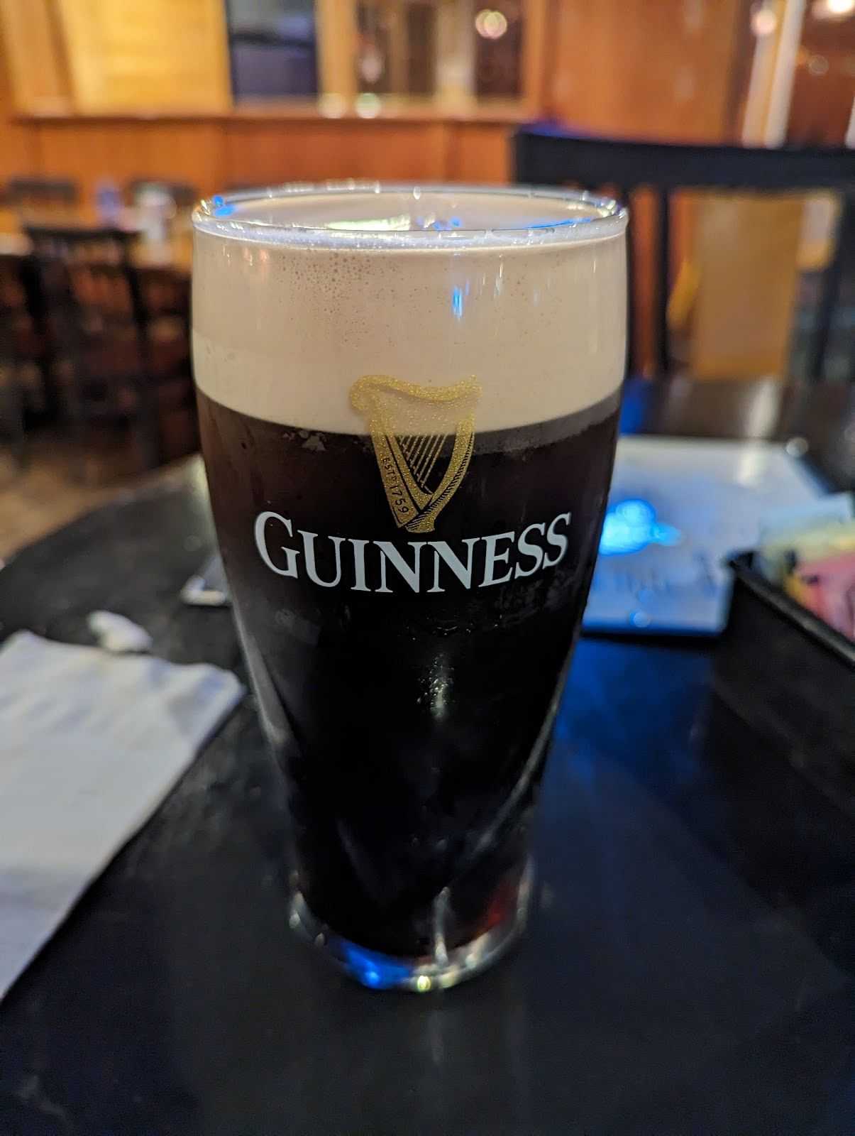 Pint of Guinness on a table in a dimly lit pub, with other tables and chairs blurred in the background.